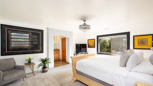 A bedroom with a large bed, a grey sofa, a small table with a plant, and artwork on the walls.