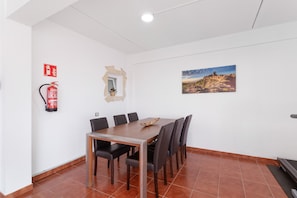 A dining area with a table, chairs, a fire extinguisher, a mirror, and a painting on the wall.