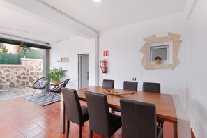 A dining area with a long wooden table, black chairs, a fire extinguisher, and a stone wall.