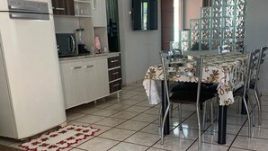 A modern kitchen with white cabinets, a refrigerator, and a microwave. There is a dining table with chairs and a floral tablecloth. - Casa Campos do Iguaçu - Perto de Tudo (Foz do Iguaçu)