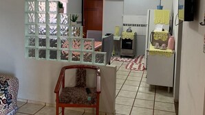 A living room with a sofa, a wooden chair, a decorative partition, a television, and a kitchen area with a refrigerator and a table. - Casa Campos do Iguaçu - Perto de Tudo (Foz do Iguaçu)