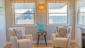 A cozy room with two plush armchairs, a small wooden side table, and a view of the sea through large windows. - Spacious, newly remodeled, canal front home located in Avon, NC. (Avon)