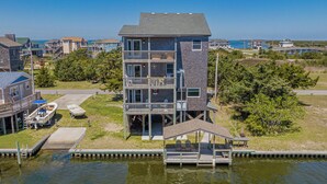 A multi-story building with a balcony, a dock, and a pier extending into the water. - Spacious, newly remodeled, canal front home located in Avon, NC. (Avon)