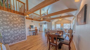 A spacious living area with a high ceiling and wooden beams, a dining area with wooden furniture, and a staircase leading to an upper level. - Spacious, newly remodeled, canal front home located in Avon, NC. (Avon)