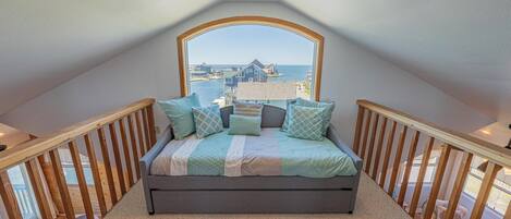 Un dormitorio con un amplio ventanal, una cama con ropa de cama estampada y vistas al frente marítimo.