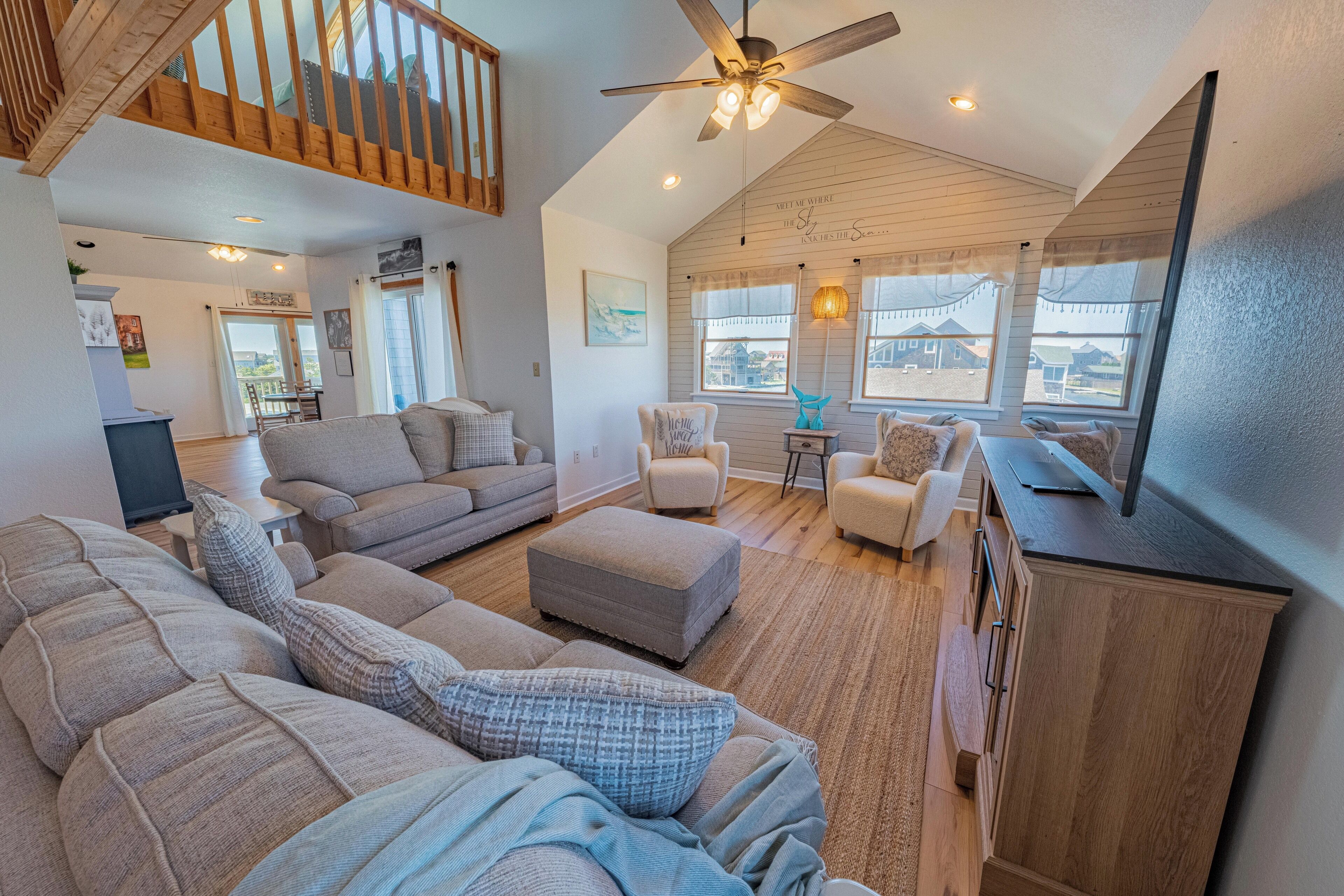 A spacious living room with a high ceiling, wooden staircase, and large windows offering a view of the outside.