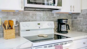 A kitchen with white cabinets, a microwave, a stove, and a coffee maker. - The Treehouse (Hakalau)