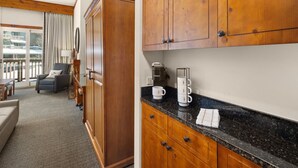 A hotel room with a seating area, wooden cabinets, a coffee maker, and a view of a balcony. - Studio Spruce Peak Ski In Ski Out "La Voûte" #147 (Stowe)