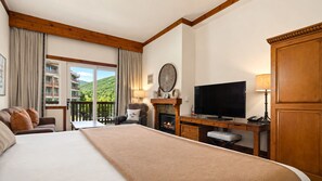 A hotel room with a large bed, a TV, a desk, and a fireplace.