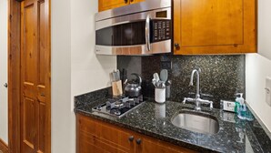 A kitchen with a stainless steel microwave, granite countertop, stainless steel sink, and wooden cabinets. - Studio Spruce Peak Ski In Ski Out "La Voûte" #147 (Stowe)