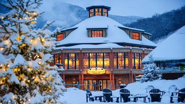 A snow-covered lodge with a central tower, large windows, and outdoor seating. - Studio Spruce Peak Ski In Ski Out "La Voûte" #147 (Stowe)