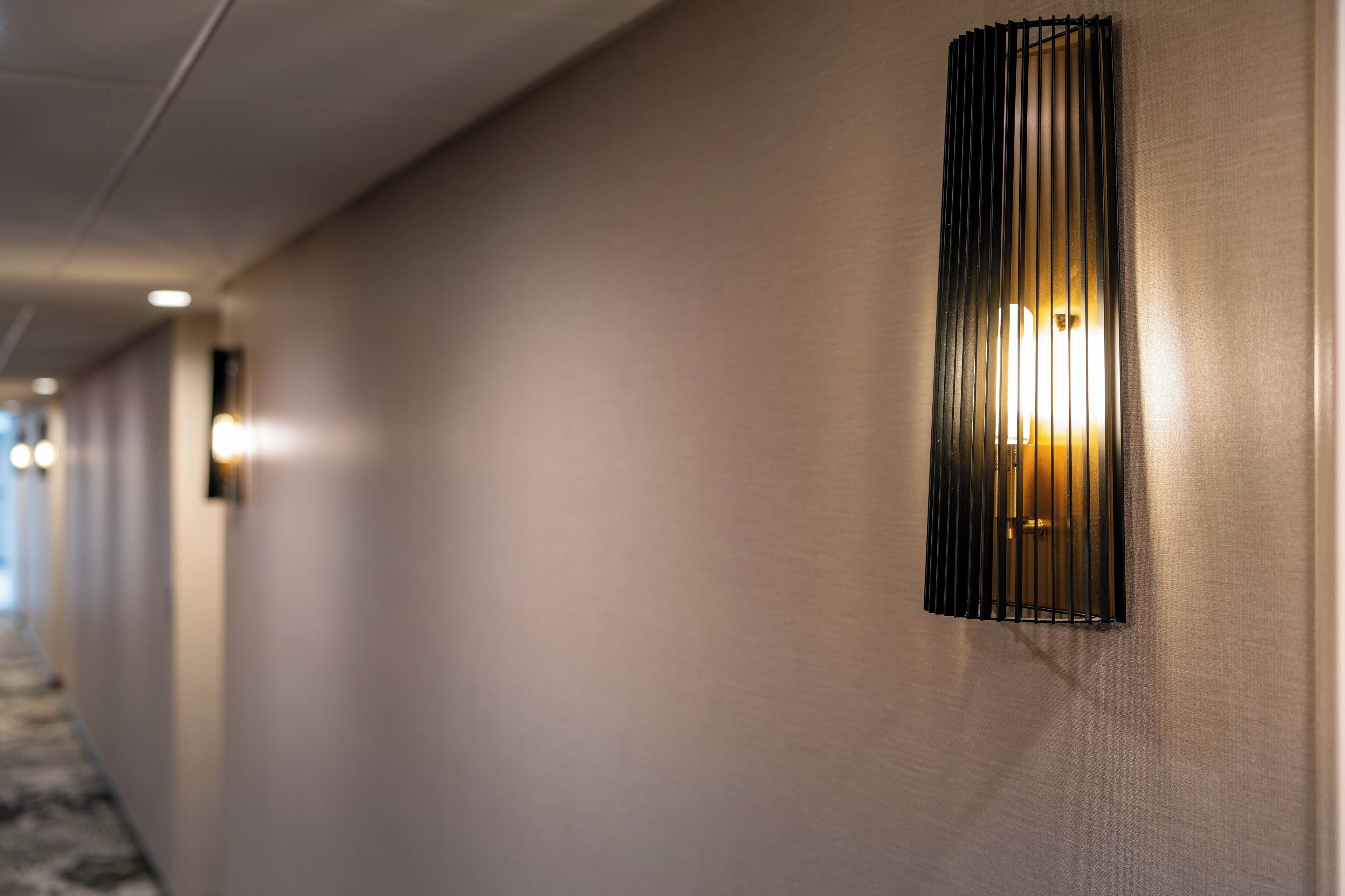 A hallway with a modern wall-mounted light fixture and a carpeted floor.