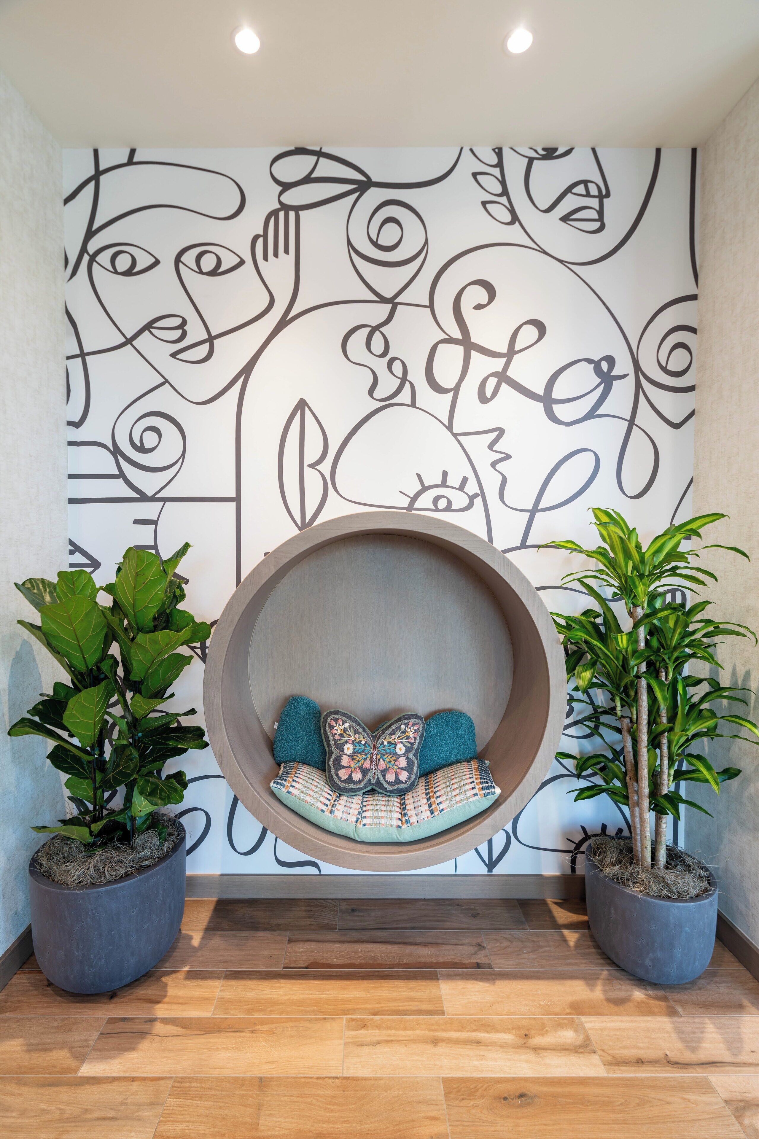 A modern interior with a unique wall art, a circular hanging seat, and two potted plants.