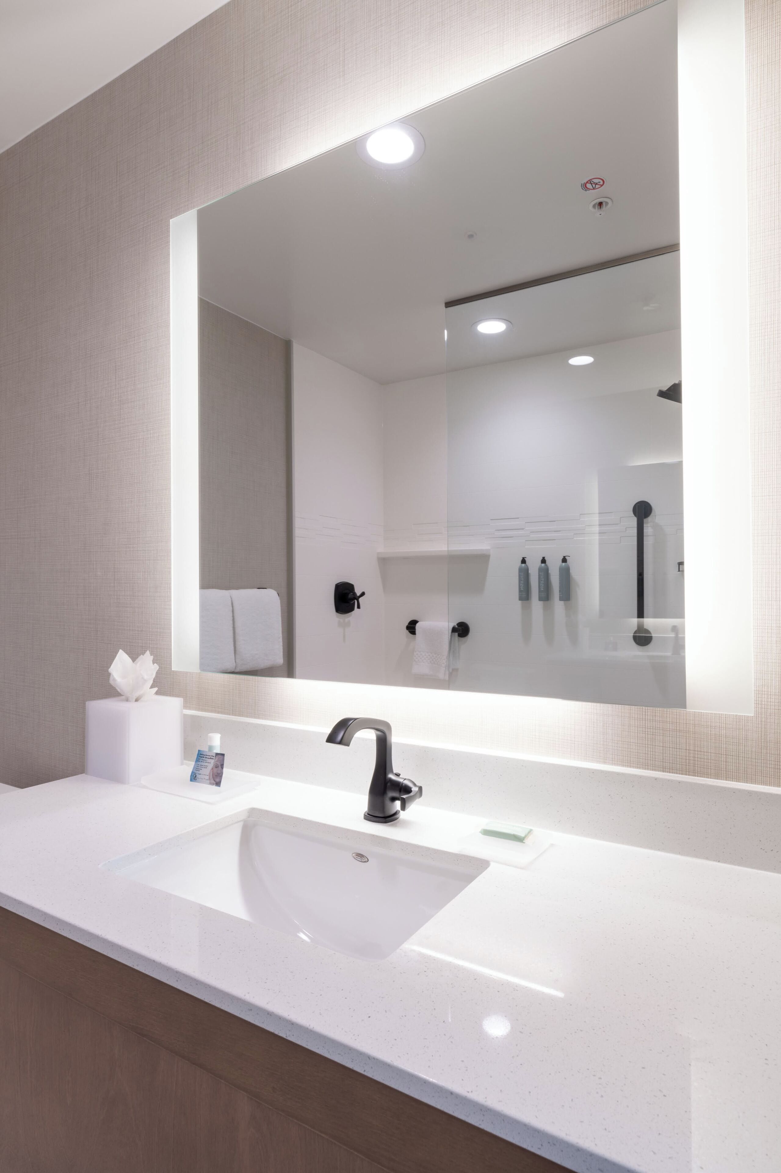 A modern bathroom with a large mirror, white sink, and a towel rack.