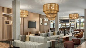 A modern hotel lobby with seating areas, large chandeliers, and a bar/lounge in the background.