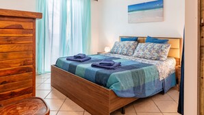 A bedroom with a wooden bed, a nightstand, a lamp, and a painting of a beach scene. - Apartment 'Le Terrazze Sul Mare - Capo' with Sea View, Private Terrace and Wi-Fi (Cefalù)