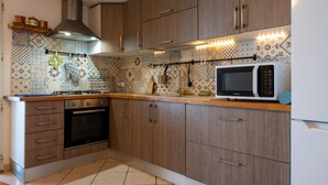 A kitchen with wooden cabinets, a gas stove, an oven, a microwave, and patterned backsplash tiles. - Apartment 'Le Terrazze Sul Mare - Capo' with Sea View, Private Terrace and Wi-Fi (Cefalù)