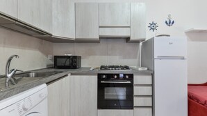 A compact kitchen with a washing machine, microwave, stove, oven, and a refrigerator. - Holiday Home 'Innamorata Mare' with Sea View, Private Terrace and Wi-Fi (Capoliveri)