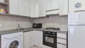A compact kitchen with a washing machine, microwave, stove, oven, and a refrigerator. - Holiday Home 'Innamorata Mare' with Sea View, Private Terrace and Wi-Fi (Capoliveri)