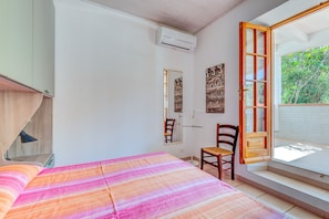 A bedroom with a bed, a chair, a window with a view of trees, and an air conditioning unit.