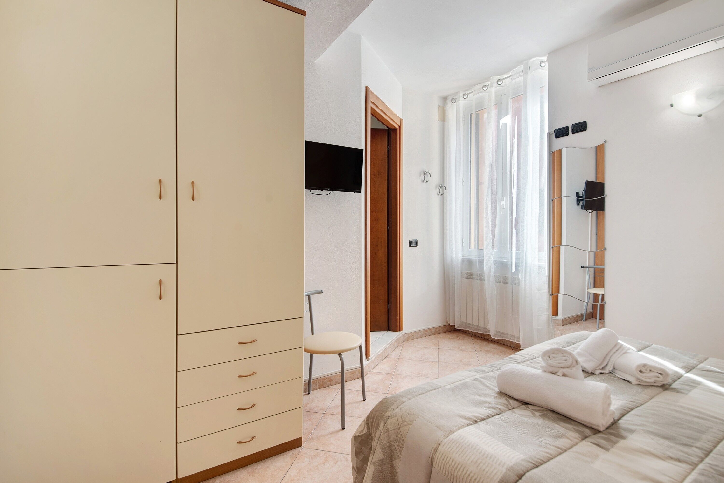 Una camera da letto con un letto, un armadio, una sedia, una televisione e una finestra con tende.