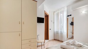 Une chambre à coucher comprenant un lit, une armoire, une chaise, un téléviseur et une fenêtre avec des rideaux.