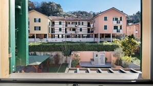Un edificio residencial de varios pisos con balcones, un pequeño jardín y vistas a una colina.