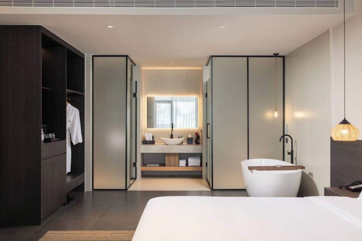 Quarto de hotel moderno com uma cama grande, guarda-roupa embutido, toucador com lavatório e banheira independente.