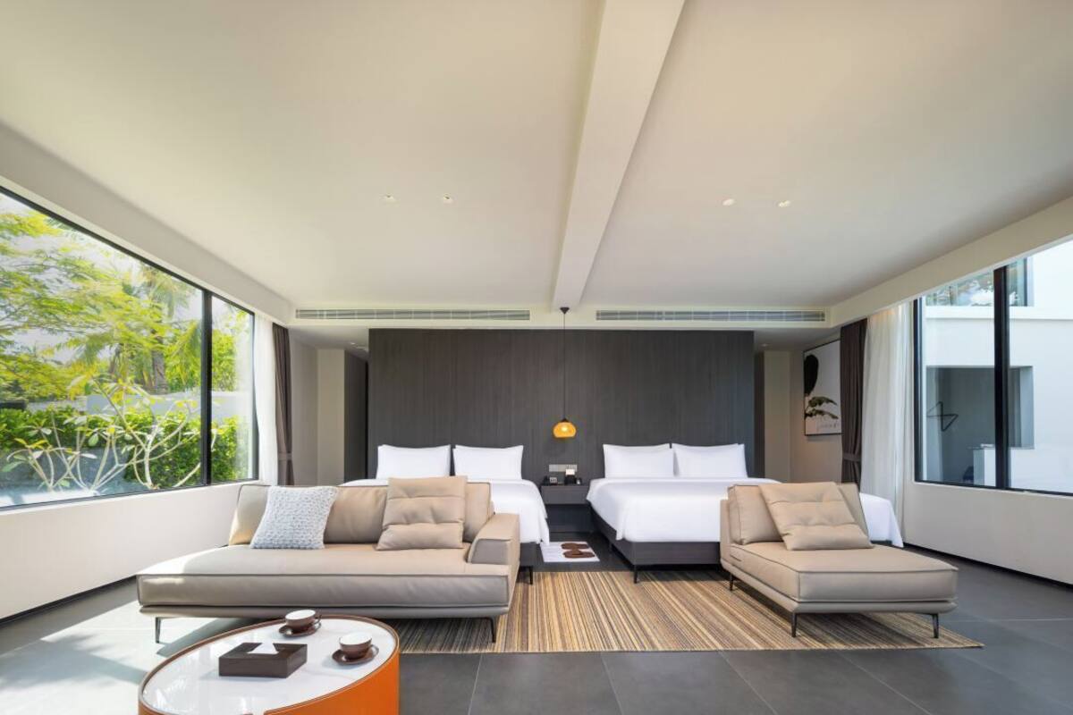 Quarto de hotel moderno com uma janela grande, duas camas, um sofá e uma mesa de centro.