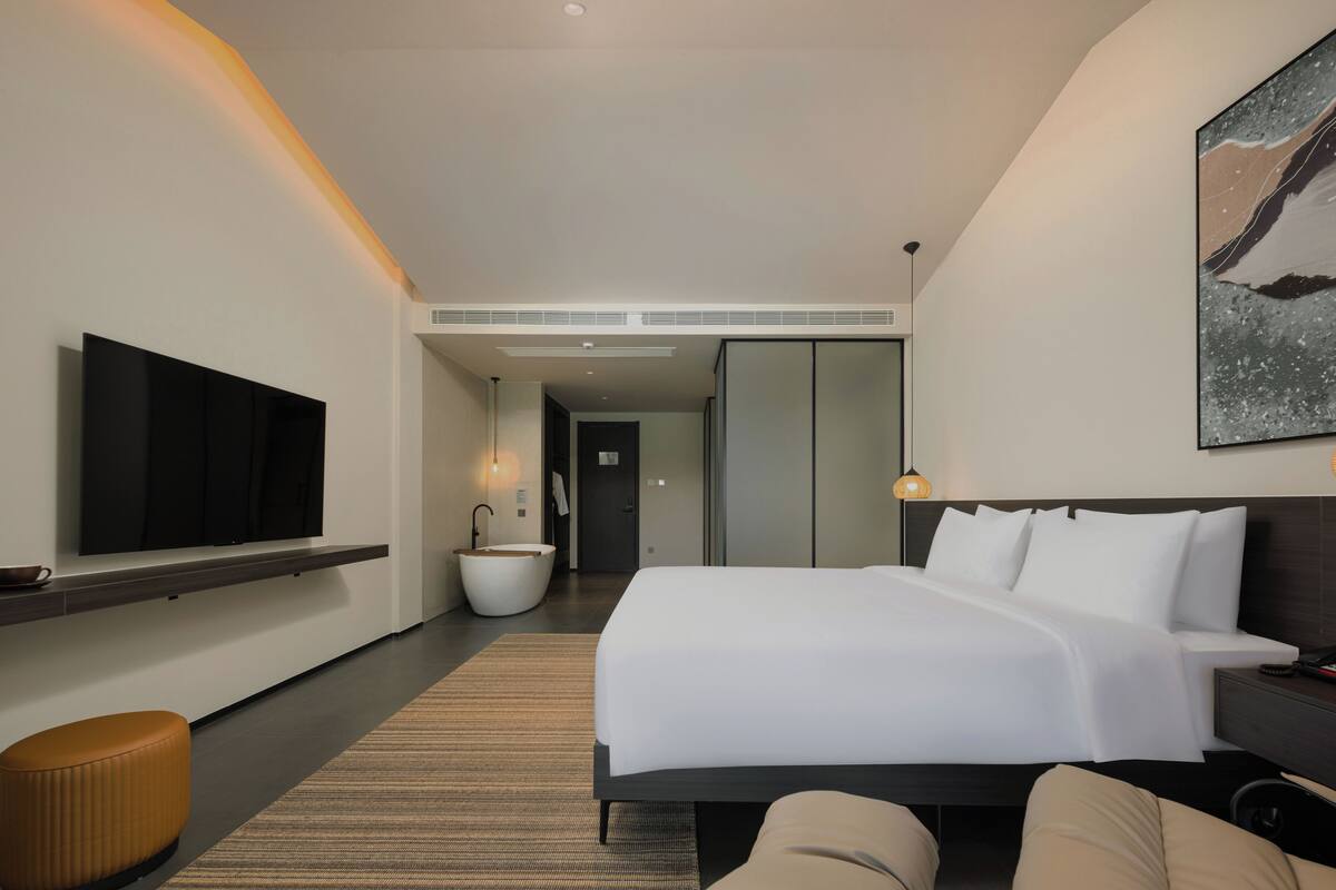 Quarto de hotel moderno com uma cama grande, televisão de tela plana na parede, área de estar circular e banheiro com uma banheira espaçosa.