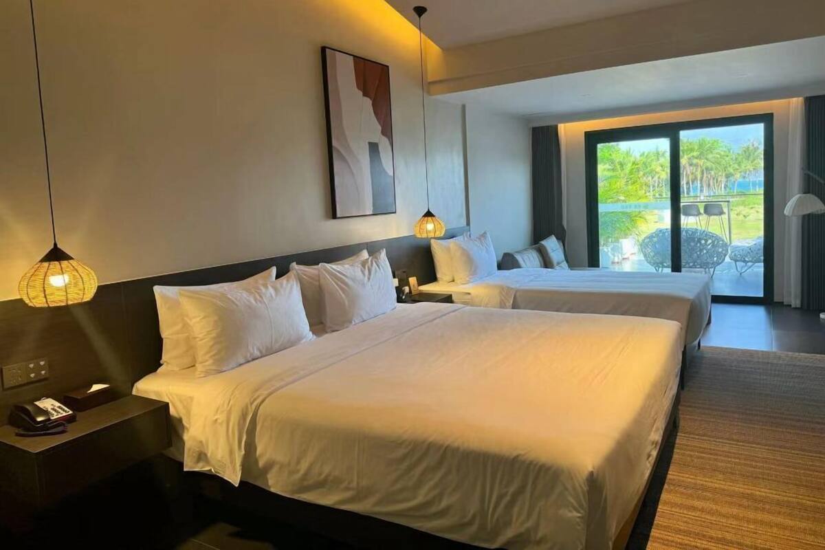 Quarto de hotel com duas camas, uma janela grande e vista para o exterior.