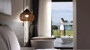 A modern hotel room with a large bed, a bedside table, a wicker lamp, and a view of a person outside. - Sanya Tufu Bay Scenic Yihai Hotel (Sanya)