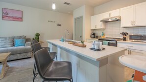 Una cocina moderna con armarios blancos, una isla central y un área de comedor con sofá y sillas.