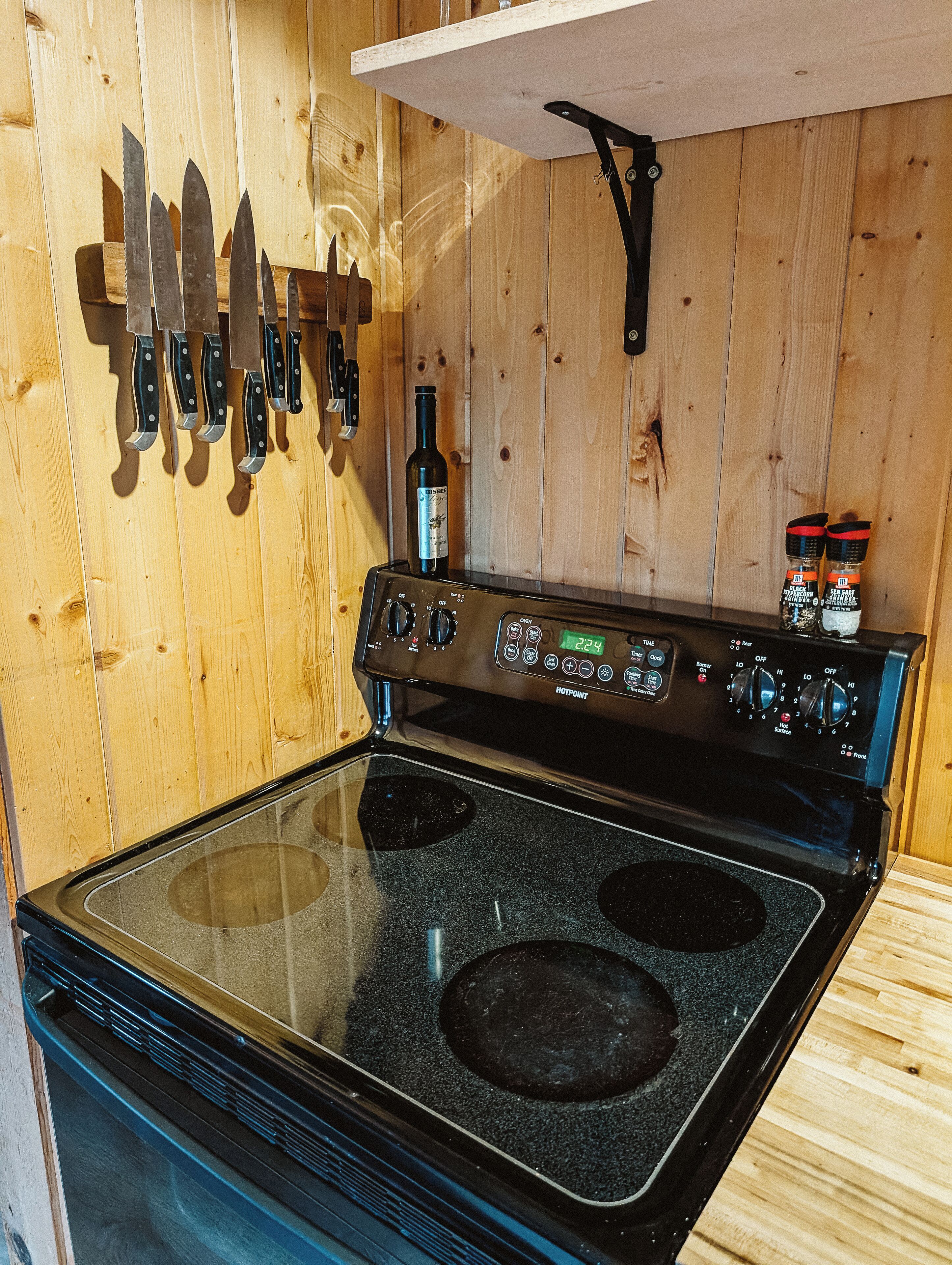 Una cucina con un piano cottura nero, pareti in legno e una bottiglia di vino sul bancone.