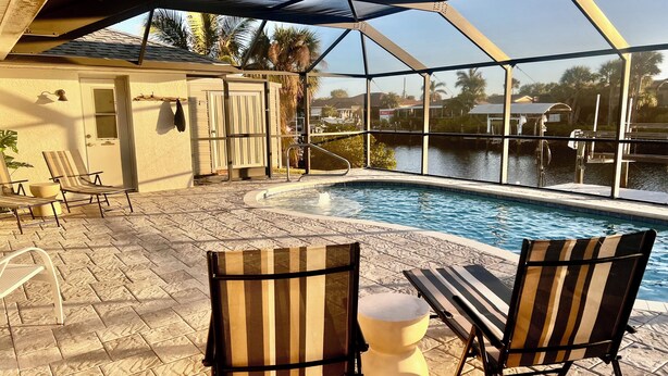Ein Poolbereich mit überdachter Terrasse, Liegestühlen und Blick auf ein Gewässer.