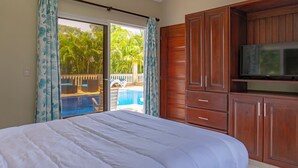 Un dormitorio con una cama grande, armarios de madera, televisión y una puerta corrediza de vidrio que da a una zona de piscina.