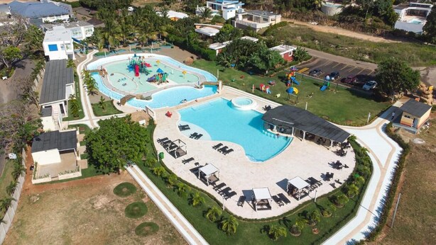 Vista aérea de un complejo turístico con varias piscinas, tumbonas y un estacionamiento.