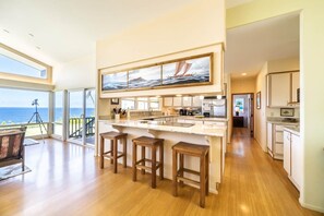 A modern kitchen with a large island, bar stools, and a view of the ocean. - The Cliffs (Hakalau)