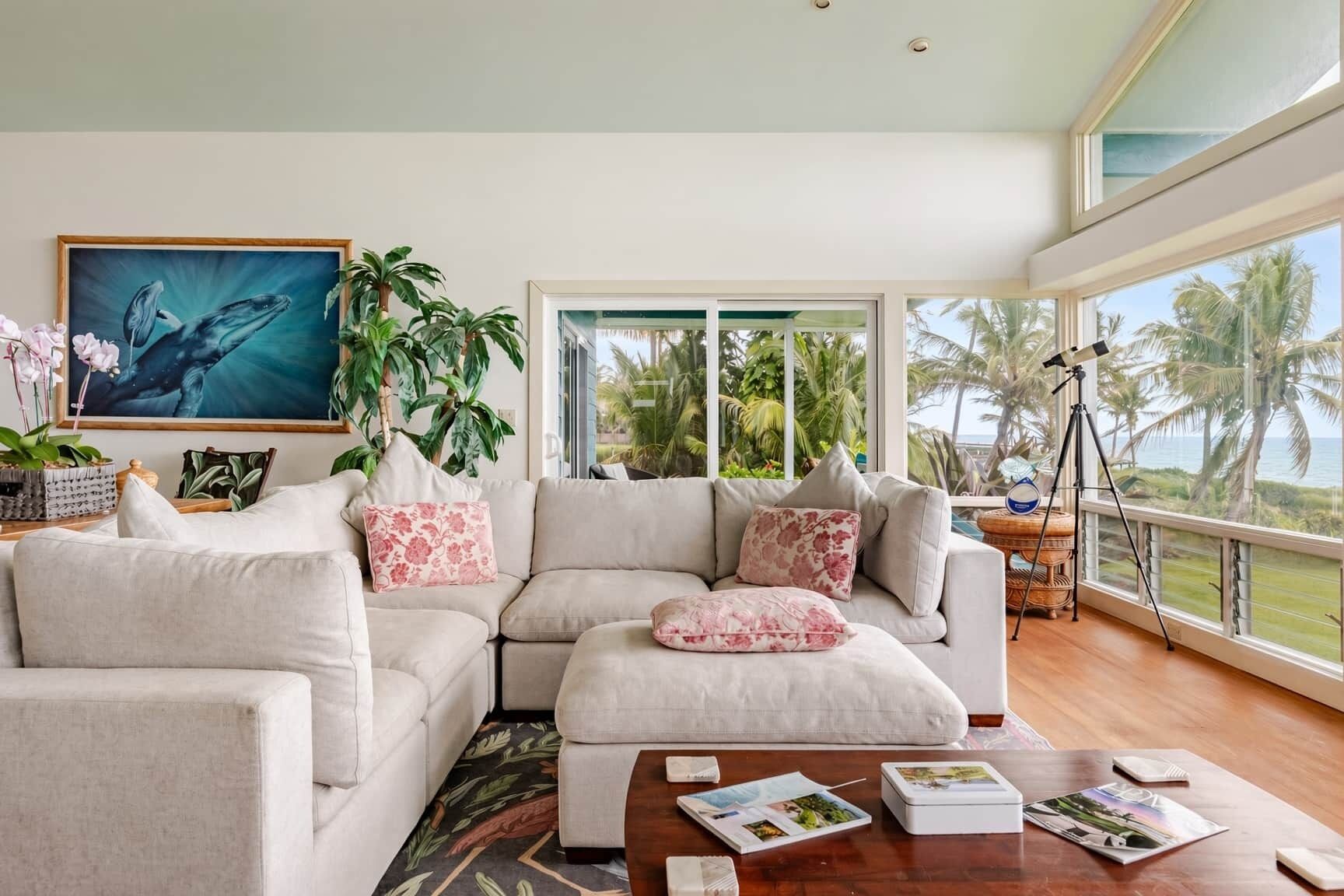 A modern living room with a large window, a sofa set, and a painting of a whale.