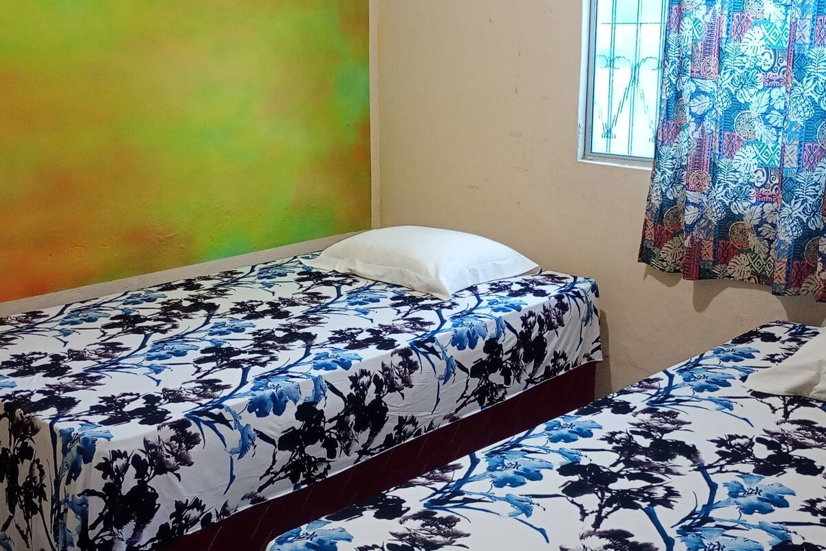 Une chambre avec deux lits, une fenêtre ornée de rideaux à motifs et un mur aux couleurs vives.