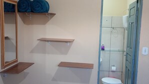 A bathroom with a toilet, a shower, and shelves with towels. - Pousada Alecrim (Santarém)