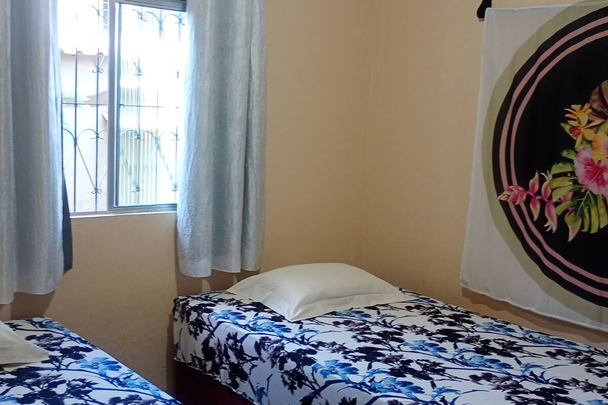 Une chambre avec deux lits, une fenêtre avec des rideaux et une tapisserie murale.