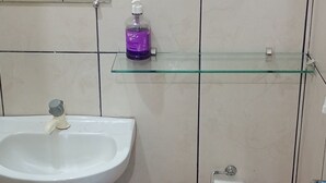 A bathroom with a white sink, toilet, and a glass shelf with a bottle. - Pousada Alecrim (Santarém)