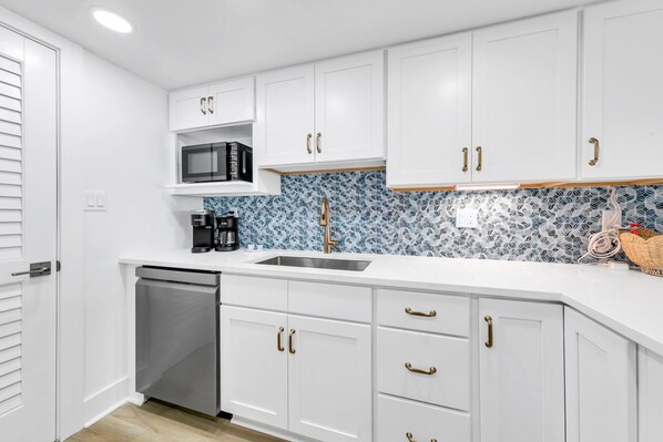 A modern kitchen with white cabinets, a stainless steel sink, a microwave, and a coffee maker.