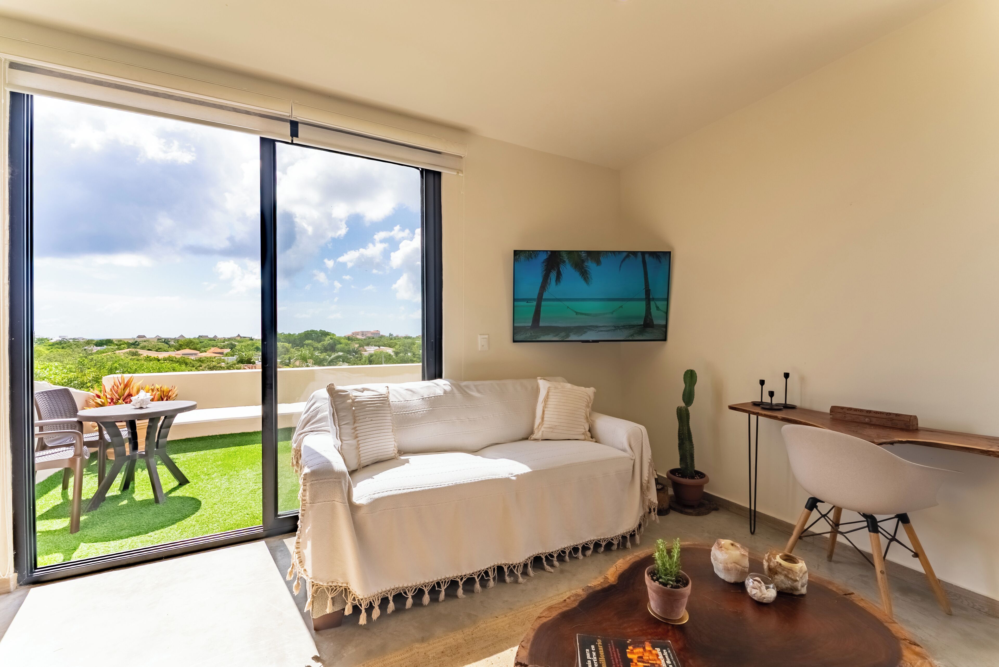 Ein modernes Wohnzimmer mit einem großen Schiebeglastür, die auf einen Balkon führt, einem weißen Sofa, einem Holztisch und einem Schreibtisch mit Stuhl.