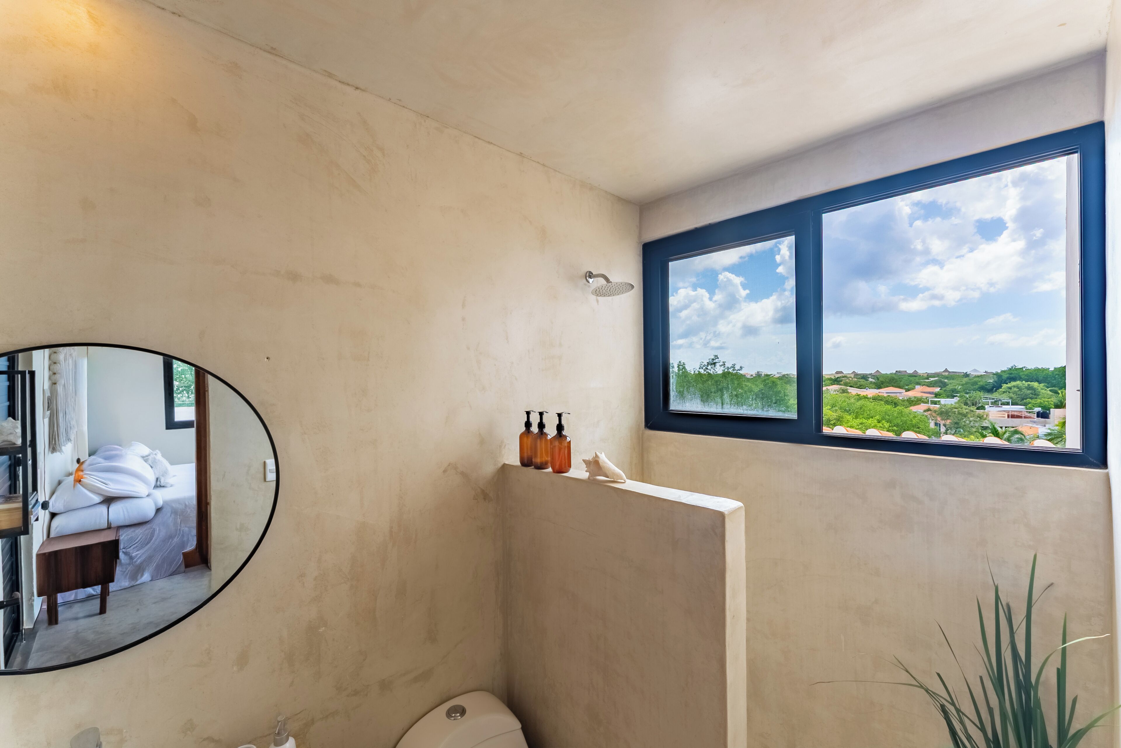 Een badkamer met een grote spiegel, een douche en een raam met uitzicht op groen en gebouwen.