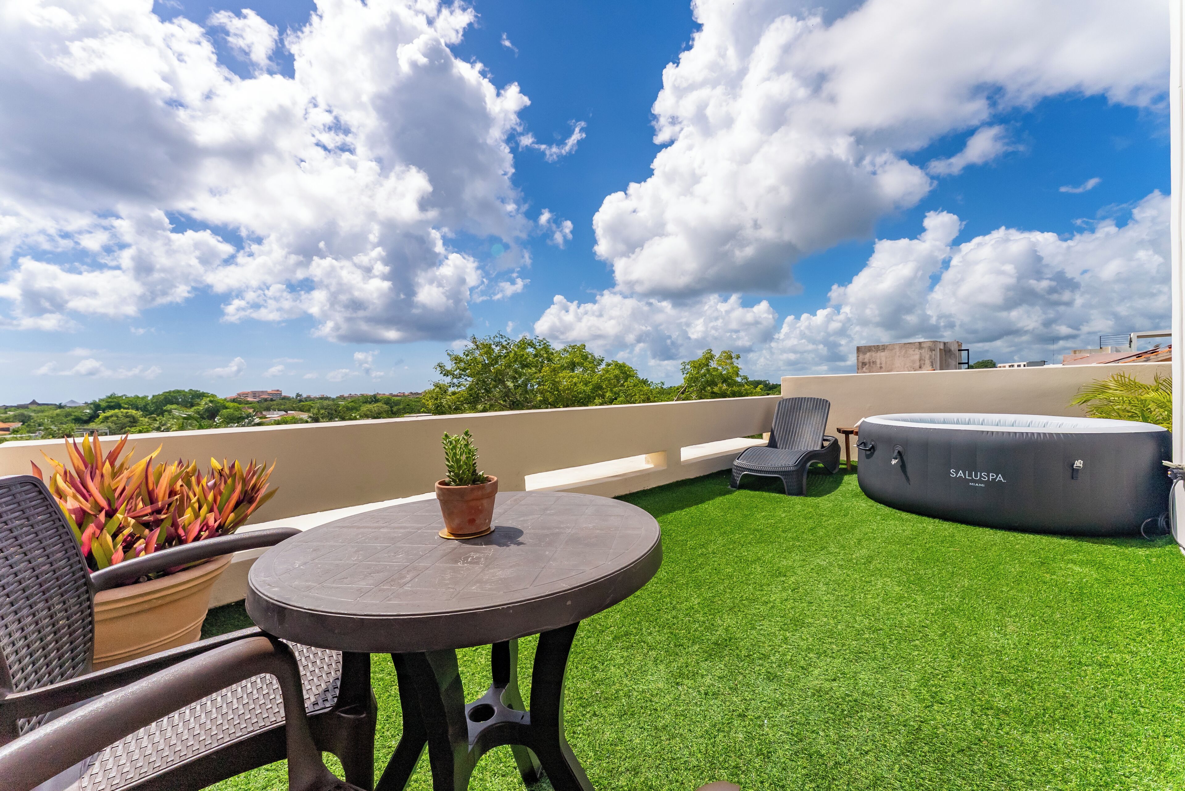 Une terrasse sur le toit avec une table ronde, des chaises, un jacuzzi et des plantes en pot.