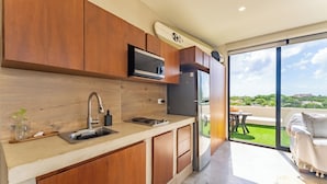 A modern kitchen with wooden cabinets, a built-in microwave, and a large window leading to a balcony with a view of the city. - Studio 55 Private HotTube (Puerto Aventuras)