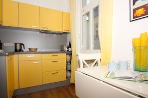 A compact kitchen with yellow cabinets, a white countertop, and a window with curtains. - Villa mit Sonnenhof - Your dream vacation in the vacation apartment Gartenzauber - Villa mit Sonnenhof (Göhren)