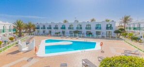 Ein Hotel mit Schwimmbad, Liegestühlen und einem weißen Gebäude mit Balkonen.